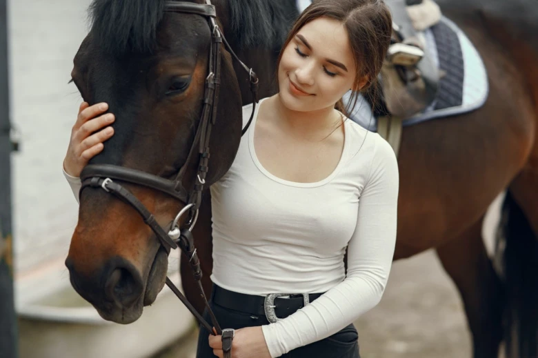 Mladá žena hladí hlavu hnědého koně v přírodním prostředí.