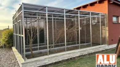 Velká venkovní voliéra pro papoušky s větvemi u domu.